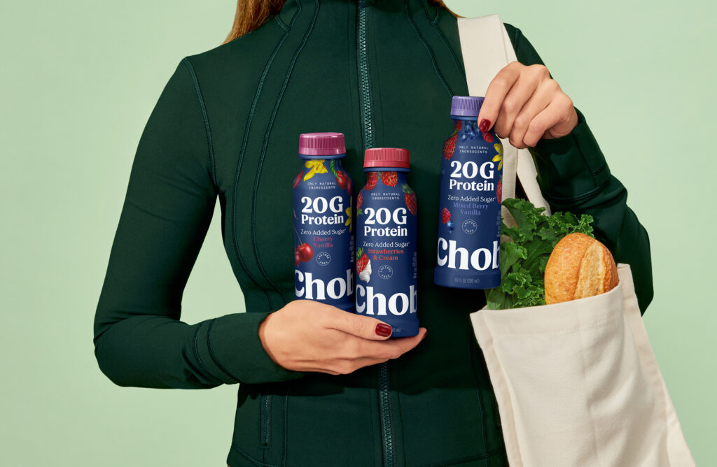 Mujer con vestimenta deportiva, con tres bebidas de yogurt Chobani en las manos.